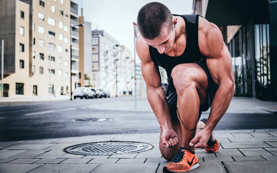 umięśniony mężczyzna wiążący pomarańczowy but nike